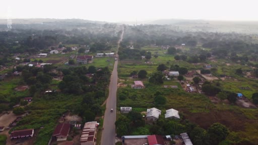 Vue aérienne plongeante montrant une route goudronnée traversant un paysage rural avec des habitations éparses et une végétation dense, illustrant les enjeux de l'aménagement du territoire et de l'accaparement des terres dans le Sud global.