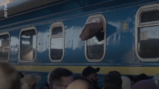 Des passagers se rassemblent sur le quai d'une gare devant un train aux couleurs bleu et jaune, évoquant les couleurs du drapeau ukrainien, lors d'une situation de crise ou d'évacuation.