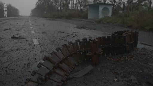 Une chenille de char métallique gît sur une route asphaltée endommagée dans un paysage de guerre, avec un abribus en arrière-plan. Cette image illustre les conséquences des combats et la destruction d'infrastructures lors d'un conflit armé.