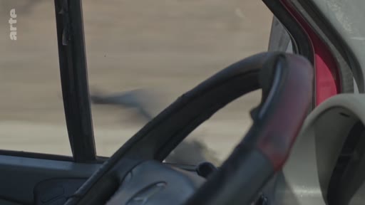 Vue subjective depuis le poste de conduite d'un véhicule circulant dans un environnement urbain en ruines, illustrant le contexte de conflit armé.