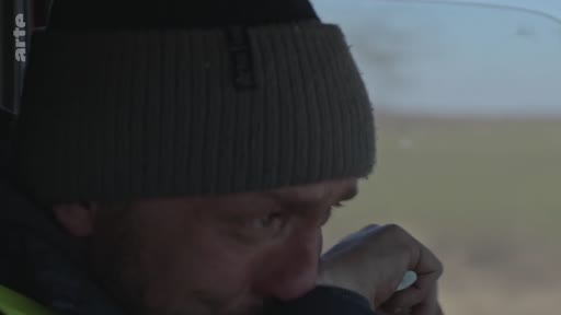 Un homme portant un bonnet gris est filmé en gros plan alors qu'il conduit, affichant une expression d'émotion ou de tristesse. Cette séquence illustre le ressenti personnel d'un individu face à une situation difficile.