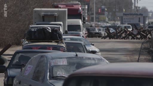 Une file de véhicules civils chargés de bagages attend à un point d'évacuation près de Zaporijia, en Ukraine, devant des obstacles antichars. La scène illustre l'exode des populations civiles fuyant les zones de conflit.