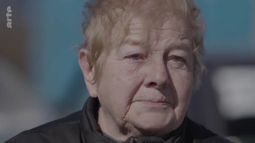 Portrait en gros plan d'une femme âgée s'exprimant lors d'une interview, évoquant son expérience de fuite face à un conflit.