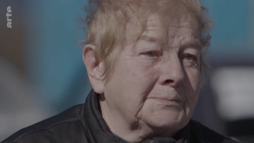 Portrait en gros plan d'une femme âgée s'exprimant lors d'une interview, évoquant son expérience de fuite face à un conflit armé.