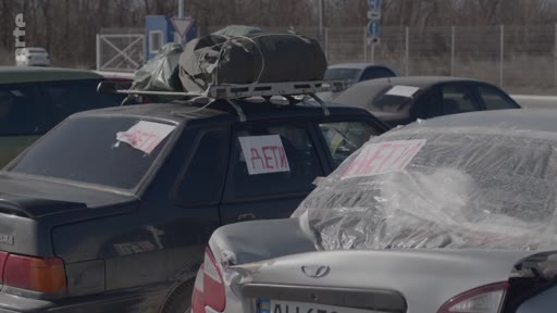 Des véhicules civils chargés de bagages, avec l'inscription « DÉTI » (enfants) apposée sur les vitres arrière, attendent lors d'une opération d'évacuation. Cette scène illustre les conditions de fuite des populations civiles en zone de conflit.