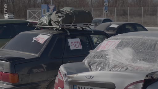 Des véhicules de civils en attente lors d'une évacuation, avec l'inscription « DÉTI » (enfants) apposée sur les vitres pour signaler la présence de mineurs à bord. Cette scène illustre les conditions de fuite des populations civiles dans un contexte de conflit.