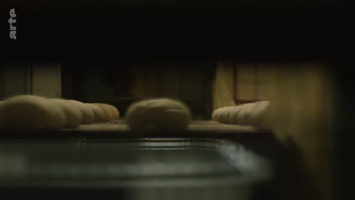 Des pâtons de pain crus sont disposés en rangées sur des plaques dans une boulangerie industrielle située près de la ligne de front, illustrant la production alimentaire en zone de conflit.