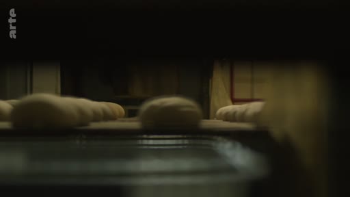 Des pâtons de pain crus sont transportés sur un tapis roulant dans une usine de production de pain, illustrant le processus de fabrication industrielle près de la ligne de front.