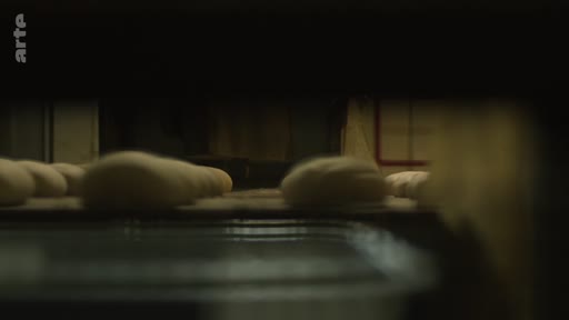 Des pâtons de pain crus sont transportés sur un tapis roulant dans une boulangerie industrielle située près de la ligne de front, illustrant la production alimentaire en zone de conflit.