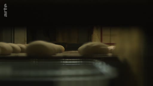 Des pâtons de pain crus sont transportés sur un tapis roulant dans une boulangerie industrielle située près de la ligne de front, illustrant la production alimentaire en zone de conflit.