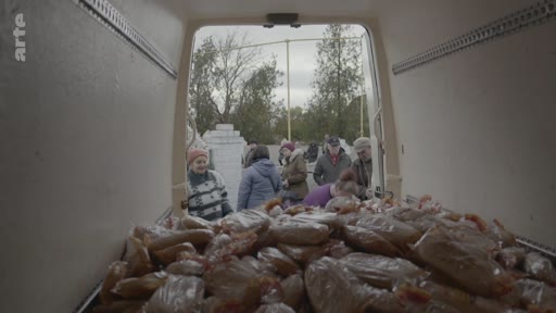Des personnes font la queue pour recevoir de la nourriture distribuée depuis l'arrière d'un camion frigorifique. Cette scène illustre une opération d'aide humanitaire ou de distribution alimentaire auprès de la population.