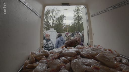 Des personnes font la queue pour recevoir de la nourriture distribuée depuis l'arrière d'un camion, dans un contexte d'aide humanitaire ou de distribution alimentaire.