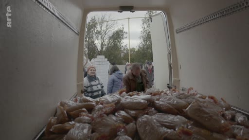 Des personnes font la queue pour recevoir de la nourriture distribuée depuis l'arrière d'une camionnette, dans un contexte d'aide humanitaire ou de distribution alimentaire.