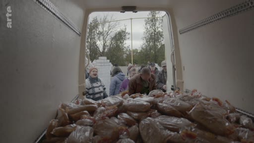 Des habitants font la queue pour recevoir des sacs de nourriture distribués depuis l'arrière d'un camion dans un contexte d'aide humanitaire ou de distribution alimentaire.
