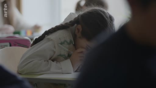 Une jeune élève avec des tresses est assise à son bureau en classe, la tête baissée, lors d'une séance de pleine conscience ou de méditation scolaire. L'ambiance est calme et studieuse dans cette salle de classe.