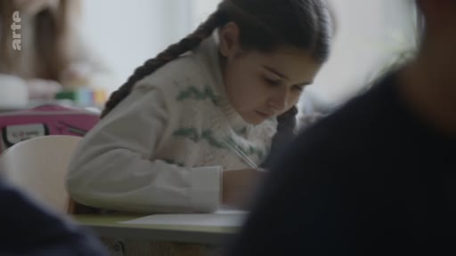 Une jeune fille avec des tresses est assise à son bureau dans une salle de classe et écrit attentivement sur une feuille de papier lors d'une séance de pleine conscience.