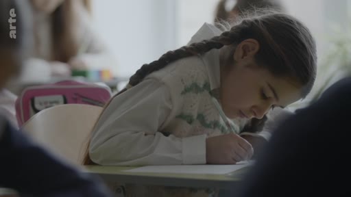 Une jeune élève avec des tresses est assise à son bureau dans une salle de classe et écrit attentivement sur une feuille de papier lors d'une séance de pleine conscience.