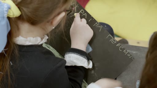 Une jeune fille écrit à la craie sur une ardoise le message « УКРАЇНА ПЕРЕМОГ » (Ukraine victoire) dans un contexte de soutien à l'Ukraine.
