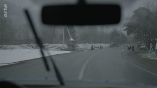 Vue subjective depuis le pare-brise d'une voiture traversant un village rural sous la neige, avec le logo de la chaîne Arte visible en haut à gauche.