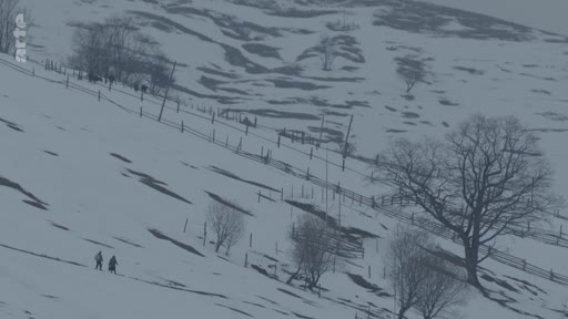 Deux personnes traversent un paysage montagneux enneigé et désolé, illustrant les conditions de vie difficiles dans une zone rurale isolée.