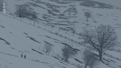 Deux individus traversent un flanc de colline couvert de neige, illustrant la vie quotidienne dans une région montagneuse ou rurale en hiver.