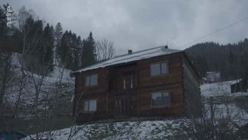 Une maison en bois à deux étages située dans un village de montagne enneigé, illustrant les conditions de vie rurales en hiver.