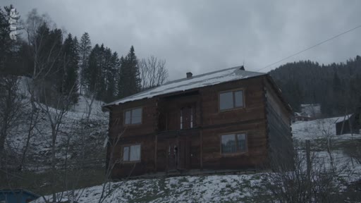 Une maison en bois isolée dans un village de montagne sous un ciel gris et un sol partiellement enneigé, illustrant la vie rurale et les conditions de vie dans les zones reculées.