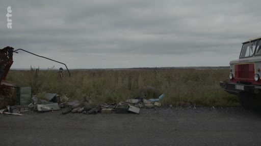 Un camion stationné sur le bord d'une route dans la région de Kherson, avec des débris et des restes de véhicules détruits au premier plan, illustrant les conséquences de la guerre en Ukraine.