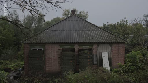 Vue extérieure d'une petite maison en briques délabrée, aux fenêtres condamnées, située dans un environnement rural ou forestier. Ce bâtiment abandonné témoigne d'un état de décrépitude avancée, typique des lieux délaissés explorés lors d'enquêtes journalistiques.