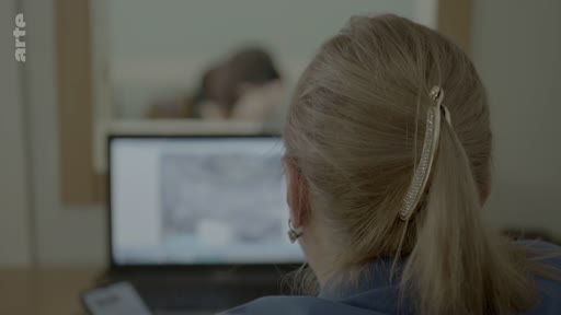 Une femme vue de dos consulte un écran d'ordinateur, illustrant le processus d'identification de victimes au sein d'un bureau de médecin légiste.