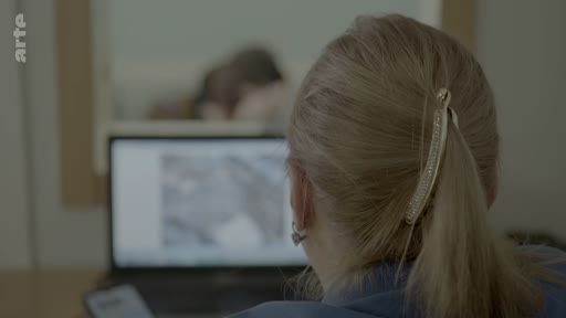 Une personne vue de dos travaille sur un ordinateur portable, probablement dans le cadre d'une enquête ou d'une identification de victimes au bureau du médecin légiste.