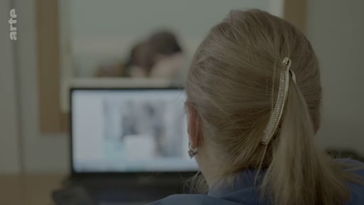 Une femme vue de dos regarde un écran d'ordinateur, dans le cadre d'une enquête sur l'identification de victimes au bureau du médecin légiste.