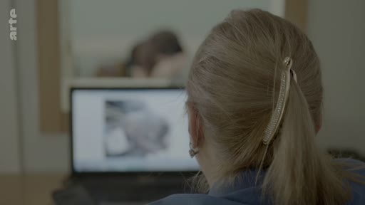 Une personne, vue de dos, examine des documents photographiques sur un ordinateur portable lors d'une procédure d'identification de victimes au sein d'un bureau médico-légal.
