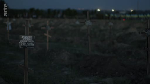 Vue d'ensemble d'un cimetière militaire à la tombée de la nuit, caractérisé par de nombreuses croix en bois marquant les tombes. Ce lieu de mémoire souligne les conséquences tragiques des conflits armés.