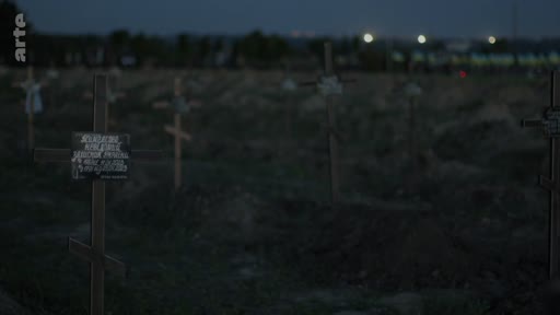 Vue d'ensemble d'un cimetière à la tombée de la nuit, caractérisé par de nombreuses croix en bois plantées dans le sol, évoquant un lieu de sépulture militaire ou de guerre.