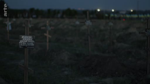 Vue d'ensemble d'un cimetière avec des croix en bois et des tombes fraîchement creusées au crépuscule, évoquant un contexte de conflit ou de tragédie humaine.