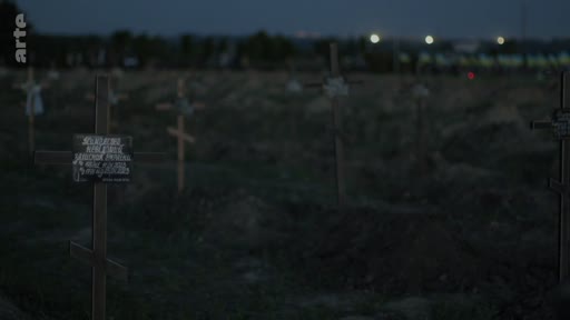 Vue d'ensemble d'un cimetière avec des croix en bois et des tombes fraîchement creusées au crépuscule, évoquant le contexte de la guerre en Ukraine. Une plaque commémorative est visible sur une croix au premier plan.