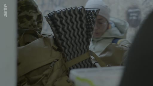 Un soldat en tenue militaire, équipé d'un sac à dos et d'un tapis de sol, arrive à son domicile. Cette scène illustre le retour au foyer d'un militaire.