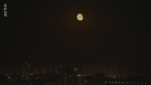 Vue nocturne d'une ville avec une pleine lune brillante dans le ciel sombre au-dessus des immeubles illuminés.