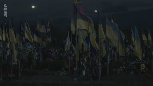 Vue d'ensemble d'un cimetière militaire en Ukraine, marqué par une multitude de drapeaux ukrainiens plantés sur les tombes, illustrant le coût humain du conflit en cours.
