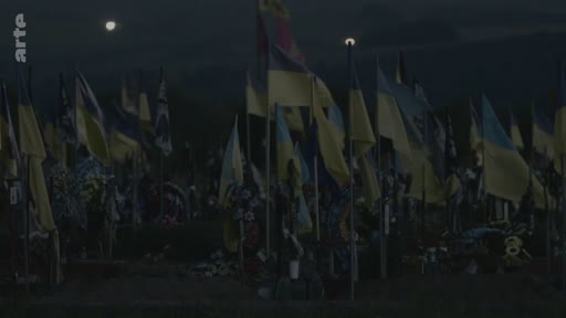Vue d'ensemble d'un cimetière commémoratif en Ukraine, marqué par une multitude de drapeaux ukrainiens flottant au crépuscule, symbolisant les hommages aux soldats tombés au combat.