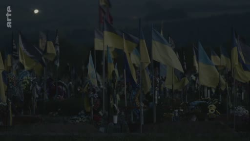 Vue d'ensemble d'un cimetière militaire en Ukraine, marqué par une multitude de drapeaux ukrainiens plantés sur les tombes sous un ciel crépusculaire. Cette image illustre le coût humain du conflit en Ukraine et le mémorial dédié aux soldats tombés au combat.