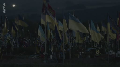 Vue d'ensemble d'un cimetière militaire en Ukraine, marqué par une multitude de drapeaux ukrainiens plantés sur les tombes, illustrant le coût humain de la guerre.