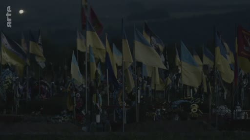 Vue d'ensemble d'un cimetière militaire en Ukraine, marqué par une multitude de drapeaux ukrainiens flottant au crépuscule, symbolisant le deuil et l'hommage aux soldats tombés au combat.