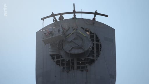 Des ouvriers utilisent une nacelle pour retirer l'emblème de la faucille et du marteau d'un bâtiment officiel, marquant la désoviétisation et la fin de l'ère soviétique.