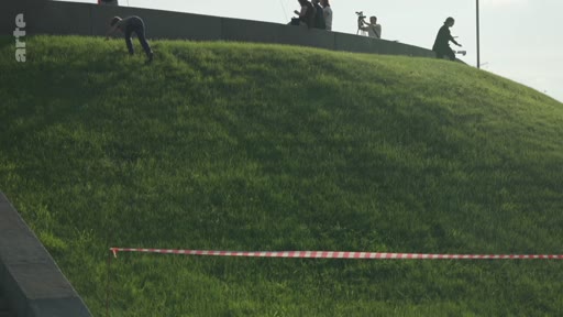 Une personne glisse sur une colline herbeuse située à proximité d'un monument, sous le regard de spectateurs en haut de la pente.