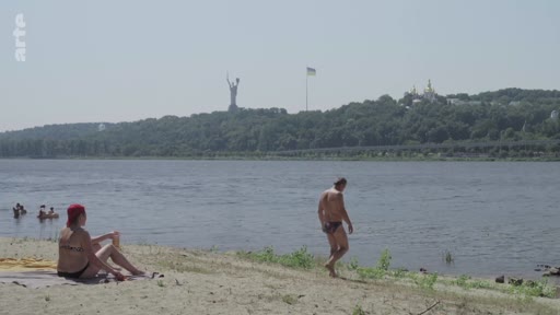 Vue d'ensemble d'une plage sur les rives du fleuve Dniepr à Kiev, en Ukraine, avec la statue de la Mère-Patrie et le monastère de la Laure des Grottes de Kiev en arrière-plan. Des personnes profitent du soleil et de la baignade par une journée d'été.