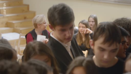 Un groupe d'élèves et une enseignante sont réunis dans une salle de classe pour une discussion interactive. L'ambiance est studieuse et participative, typique d'un environnement scolaire.