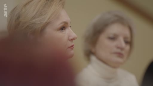 Deux femmes, dont l'une est au premier plan, assistent à une discussion ou une conférence dans le cadre d'un reportage sur l'éthique du rêve en temps de guerre.