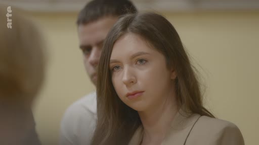 Une jeune femme ukrainienne participe à une discussion sur les visions étudiantes pour l'avenir de l'Ukraine, filmée dans un cadre formel. Elle est accompagnée d'un autre étudiant en arrière-plan, illustrant les préoccupations de la jeunesse ukrainienne face aux enjeux actuels.